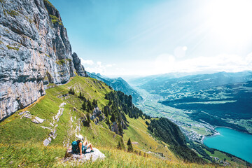 Sporty woman sits on a rock next to the hiking trail and enjoys the view of lake Walensee and...