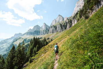 Athletic woman walks on scenic hiking trail between meadow and trees and the Churfürsten mountain range in the background. Schnürliweg, Walensee, St. Gallen, Switzerland, Europe.