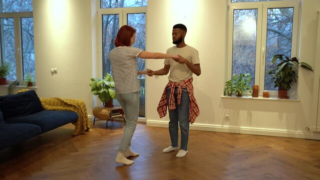 Loving romantic diverse multiethnic couple dancing to favorite music in living room together. Carefree interested black husband and european wife enjoy weekend time flirting having fun at home