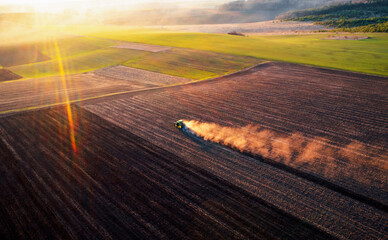 A cloud of dust rises behind a tractor plowing the ground.