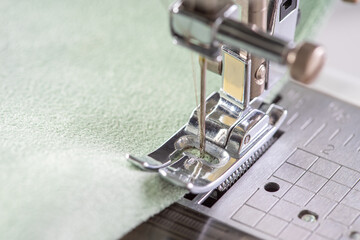 Modern sewing machine presser foot with green fabric and thread, closeup, macro