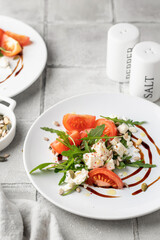 Healthy vegetable salad with fresh arugula, tomato, feta cheese on white plate served for two, gray tile background. Diet menu. Appetizer salad