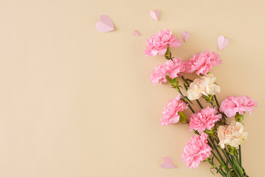 Beautiful Mother's Day floral arrangement concept. Top view photo of bouquet of pink white carnation and paper hearts on light beige background. Flat lay with empty space for greeting text or advert