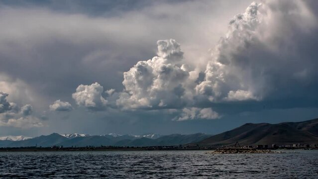 Time lapse of rapid formation and movement of clouds and blue clouds over a mountain lake or sea with picturesque mountain shores. Accelerated movement of clouds and water waves