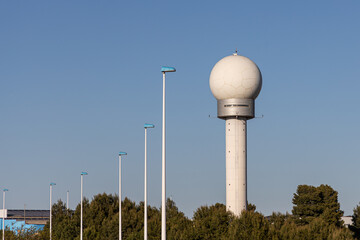 Gray metal ball-shaped location antenna tower is on the blue sky background with green trees in sunny day