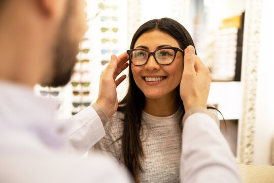 Happy woman trying on different eyeglass frames in store