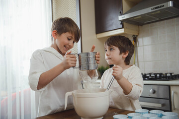 Two little boys, brothers make homemade cupcakes in the kitchen. Family creativity, hobbies, joint activities with children. Siblings cooking.