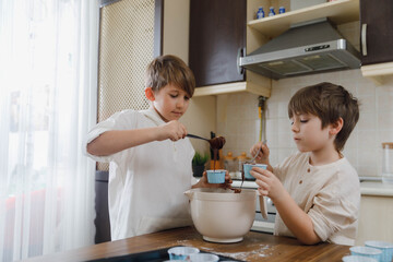 Family activities for kids at home. Two little boys, brothers having fun making homemade cupcakes,...