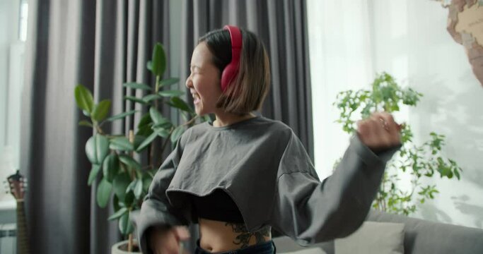 Asian woman playing air guitar and wearing headphones to listen to music, having fun at home