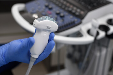 Close-up of ultrasound diagnostic probe. A doctor's hands hold a transducer with gel for diagnosing internal organs using modern ultrasound technology, including elastography and sonography.