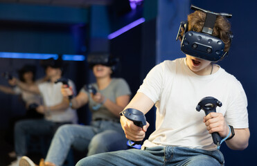 Young guy with handheld controllers in hands clearly excited and engaged in virtual world experiencing through VR glasses covering face. Concept of immersion and interactivity in game