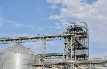 Some equipment of modern sugar factory, metal structures, tower and top of a big vat (tank), blue sky with white clouds, panoramic image