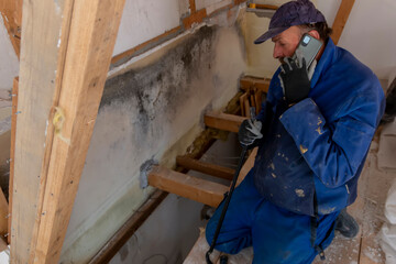 A  worker is holding a phone and talking while working on a house renovation..Preparation for...