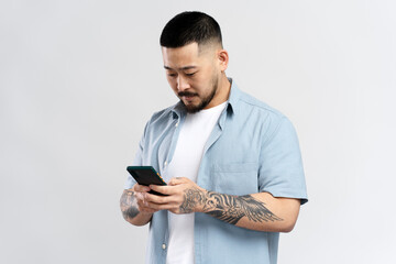 Handsome asian man with stylish tattoo holding mobile phone reading text message, communication...