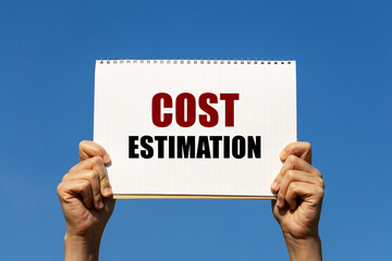 Cost estimation text on notebook paper held by 2 hands with isolated blue sky background. This message can be used as business concept about cost estimation.