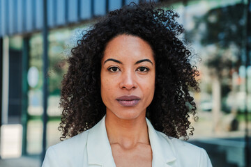 Serious african american businesswoman looking pensive at camera with proud attitude wearing a executive suit Close up portrait of hispanic corporate female worker with curly hair standing at worplace