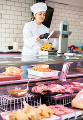 Young female butcher weighing whole chickens on scales in butchery