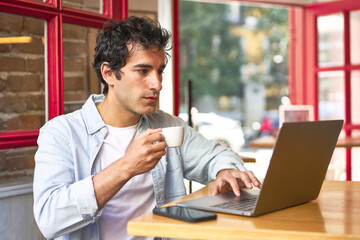 Young man concentrates on work with laptop at cozy cafe.