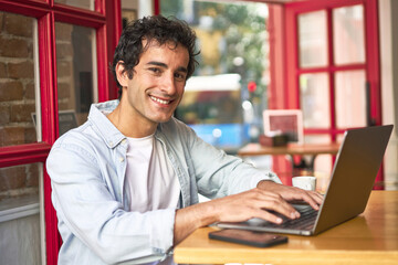 Caucasian millennial happily browsing on laptop at cozy cafe.