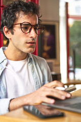 Young man takes notes while working on laptop at cozy cafe.