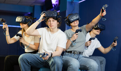 Exited from virtual spaceship flight game, excited teenager sits next to three friends. student with vr headset on forehead and analog stick sits next to gamer friends