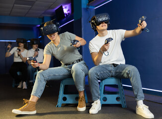 Excited couple, young girl and guy, with handheld controllers in hands engaged in virtual world...