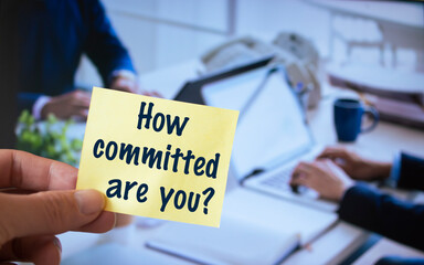 Male hand holding sticky note written How Committed Are You?