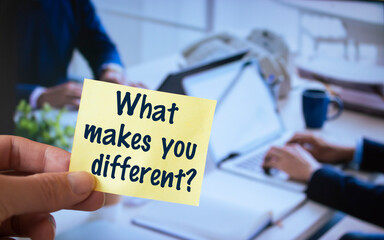Male hand holding sticky note written What Makes You Different?