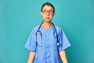 A young nurse woman isolated shrugs shoulders and open eyes confused.