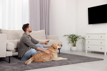 Man turning on TV near his cute Labrador Retriever at home. Space for text