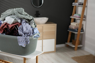 Laundry basket filled with clothes on table in bathroom. Space for text
