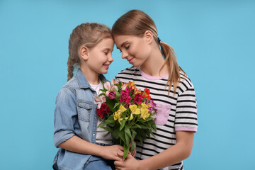 Fototapeta na wymiar Little daughter congratulating her mom with flowers on light blue background. Happy Mother's Day