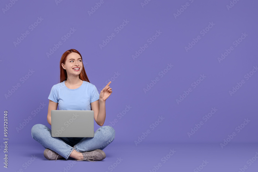 Wall mural Smiling young woman with laptop on lilac background, space for text