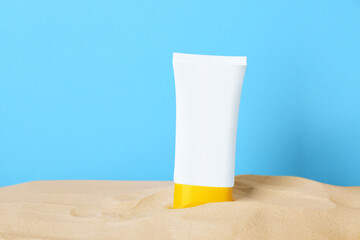 Suntan product in sand against light blue background. Space for text