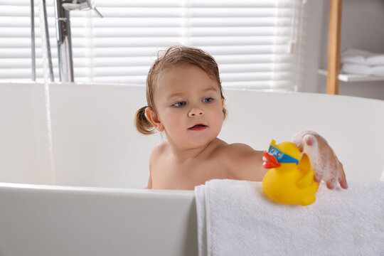 Cute little girl taking bath with toy indoors