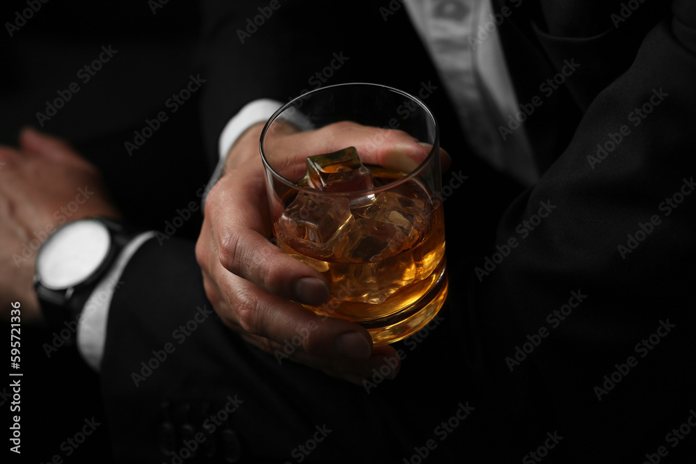 Poster Man holding glass of whiskey with ice cubes on black background, closeup