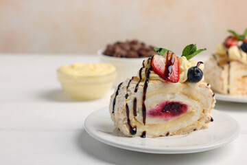 Piece of tasty meringue roll with jam, cream, strawberry, blueberry and mint on white wooden table, closeup. Space for text