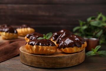 Delicious profiteroles with chocolate spread and mint on wooden table, closeup