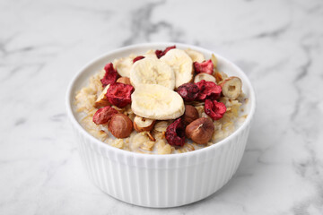Delicious oatmeal with freeze dried berries, banana and hazelnuts on white marble table, closeup