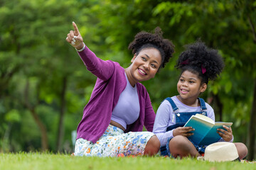 African American teacher is teaching her young student to read while having a summer outdoor class in the public park for education and happiness concept
