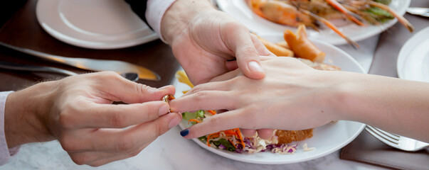 Closeup hands of man putting ring on finger of woman for marriage or engagement together with surprise at restaurant luxury, love and fiance, anniversary and celebrate, affectionate and bonding.