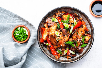 Stir fry chicken fillet, red paprika, mushrooms, green chives and sesame seeds in ceramic bowl Asian cuisine dish. White kitchen table background, top view