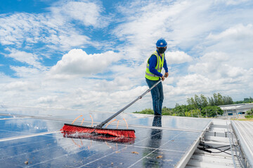 Professional worker cleaning solar panels with brush and washing with water on roof structure of...