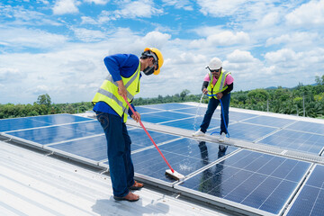 Professional worker cleaning solar panels with brush and washing with water on roof structure of...