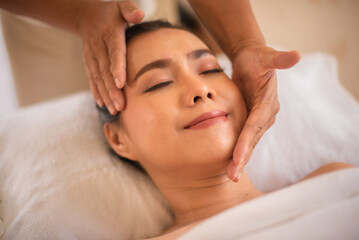 Fototapeta na wymiar Beautiful asian client gets head and chin massaged with happy expression by professional masseuse