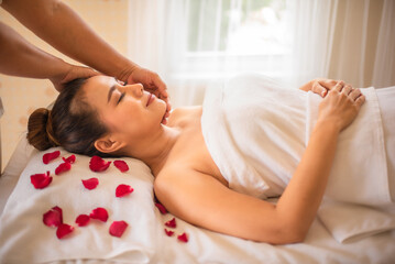 Obraz na płótnie Canvas Beautiful asian woman closes her eyes relaxation as the masseuse works on a bed strewn with rose petals.
