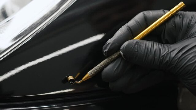 Gloved hand applying touch-up paint with a gold fluid writer pen on a black car. High quality 4k footage