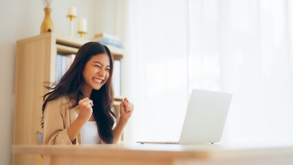 Funny euphoric young asian woman celebrating winning or getting ecommerce shopping offer on computer laptop. Excited happy girl winner looking at notebook celebrating success - obrazy, fototapety, plakaty