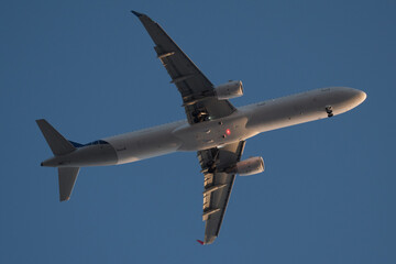 Fototapeta na wymiar vista inferior del fuselaje de un avion comercial proximo al aterrizaje iluminado por el sol del atardecer