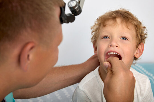 An otolaryngologist uses a wooden spatula to check the condition of the child's palatine tonsils. Cute boy opened his mouth wide so that the doctor would check the adenoids